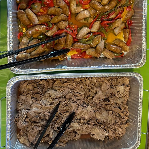 Two foil pans of catering food: sausage and peppers, and thinly sliced roast beef.