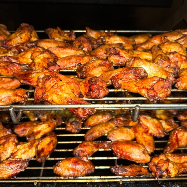 Rows of golden-brown chicken wings cooking on a metal grill rack, ready for Top Butcher Market customers.