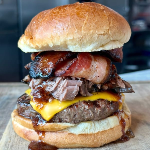 A towering Top Butcher Market burger with cheese, pulled pork, and bacon on a bun.