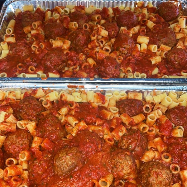 Two foil pans filled with rigatoni pasta and meatballs in a rich red tomato sauce.