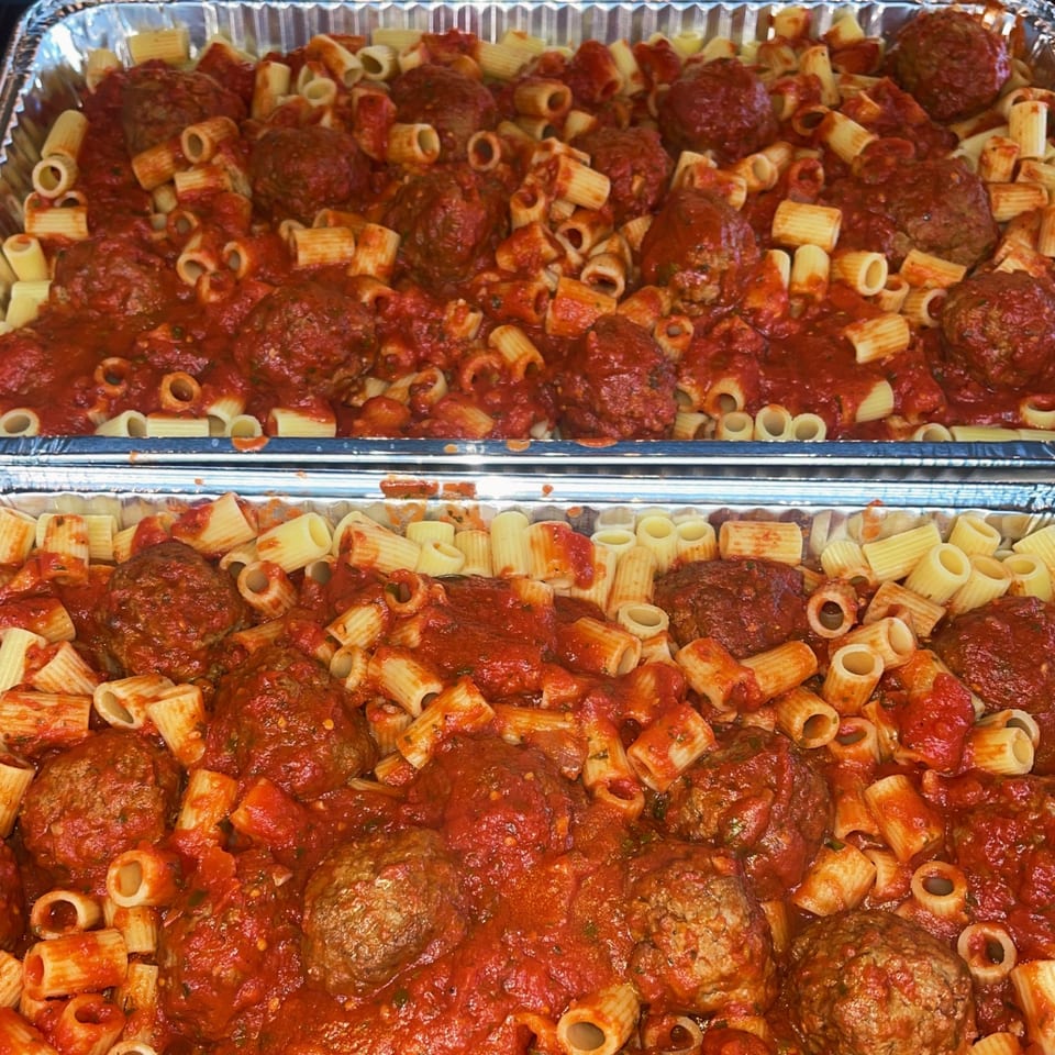 Two foil pans filled with rigatoni pasta and meatballs in a rich red tomato sauce.