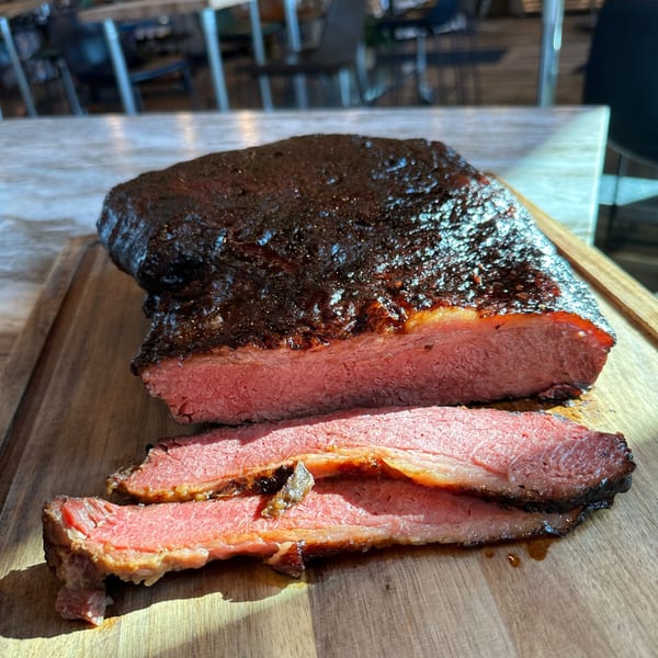 A large, dark-crusted brisket, partially sliced to reveal its tender, pink interior on a wooden board.