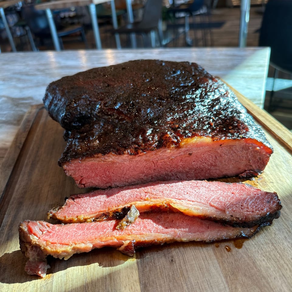 A large, dark-crusted brisket, partially sliced to reveal its tender, pink interior on a wooden board.
