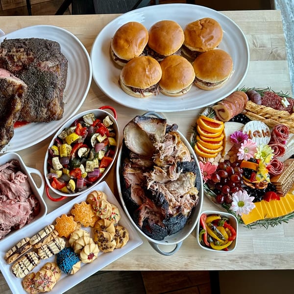 A Top Butcher Market feast with prime rib, pulled pork, sliders, roasted vegetables, and a dessert platter.