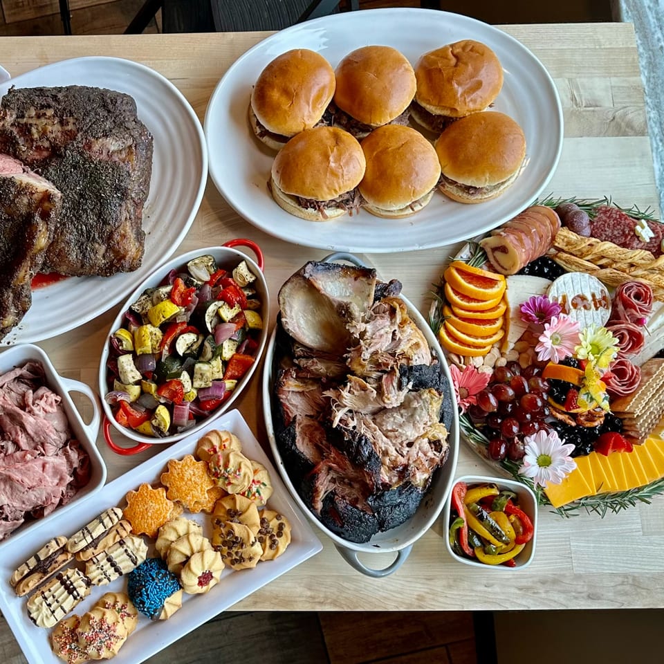 A Top Butcher Market feast with prime rib, pulled pork, sliders, roasted vegetables, and a dessert platter.