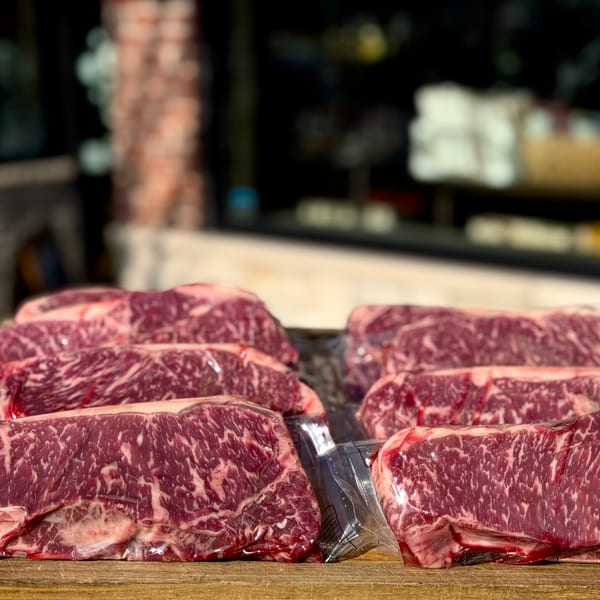 Vacuum-sealed cuts of marbled raw beef, likely New York strips, on a wooden surface at Top Butcher Market.