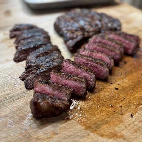 Two perfectly cooked, sliced steaks with a pink center, seasoned with salt and pepper on a wooden board.